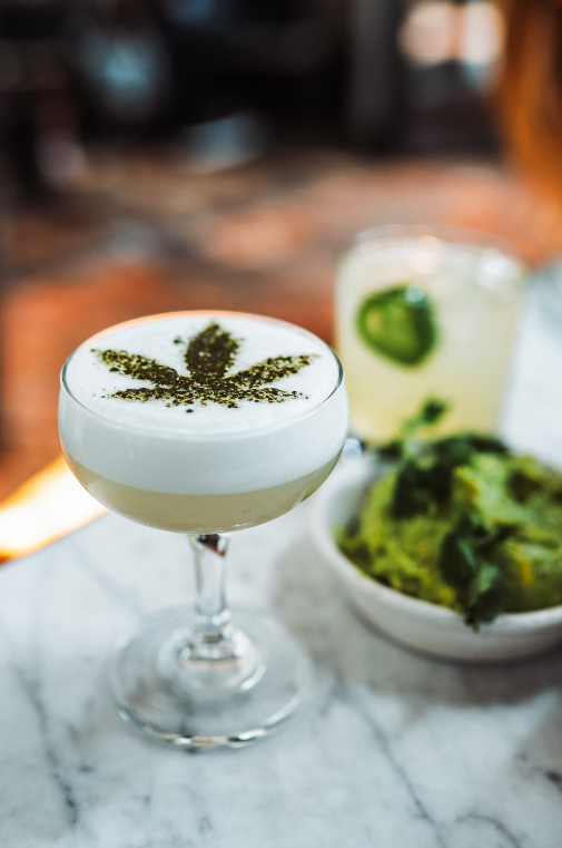 A champagne glass containing a cocktail that has a marijuana leaf stenciled on top