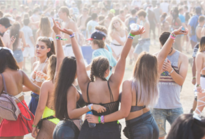 Three young women pose for a photo with their backs to the camera. A crowd surrounds them