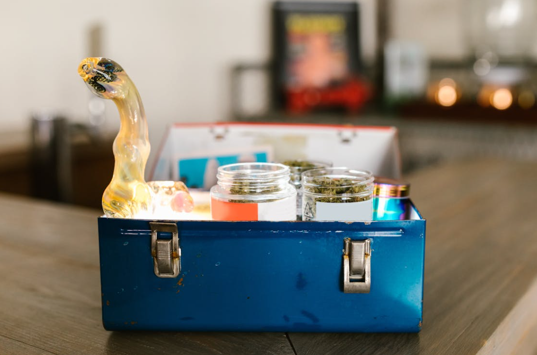 Cannabis in jars and a glass pipe in a blue metal box