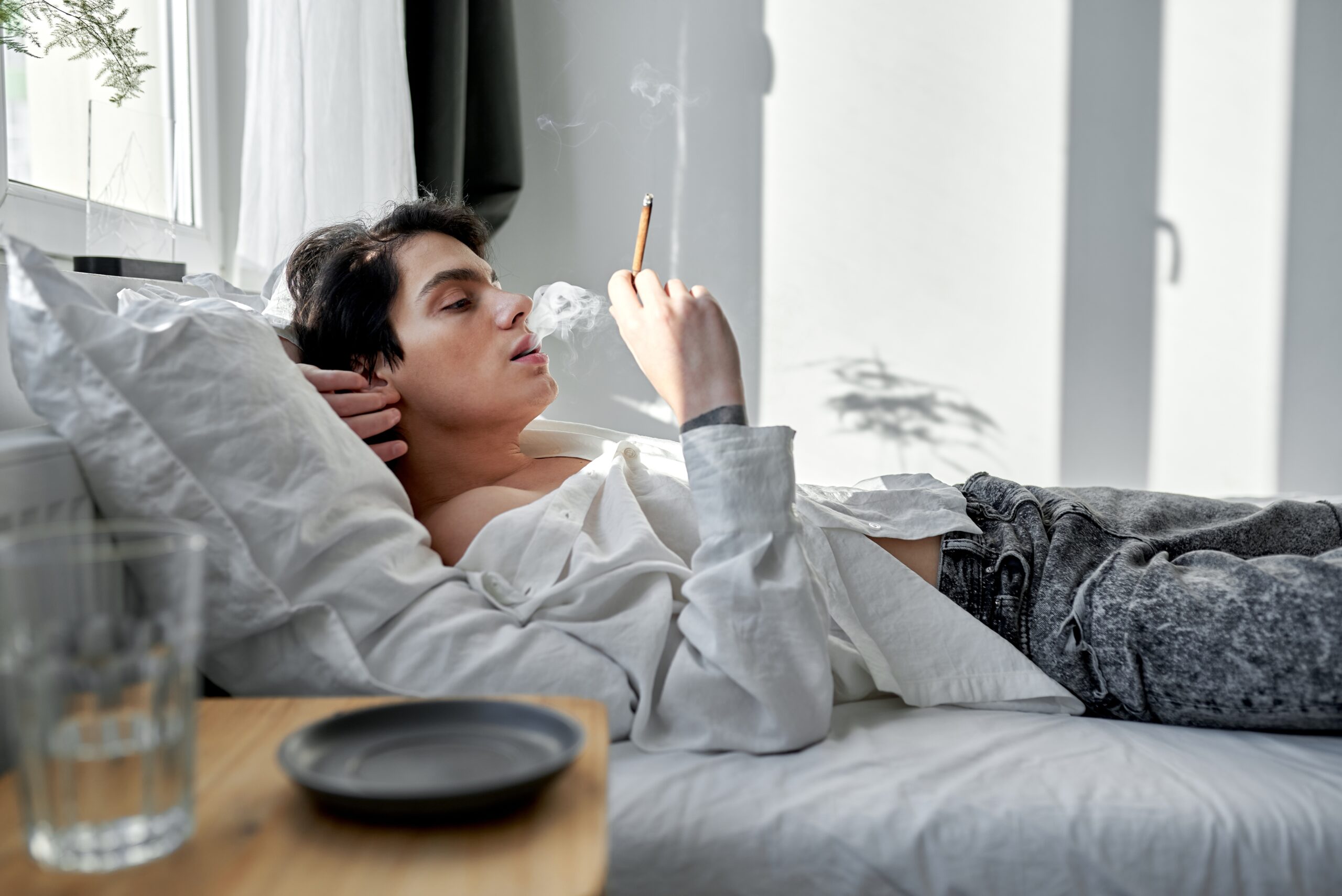 Young man smoking and relaxing in bed